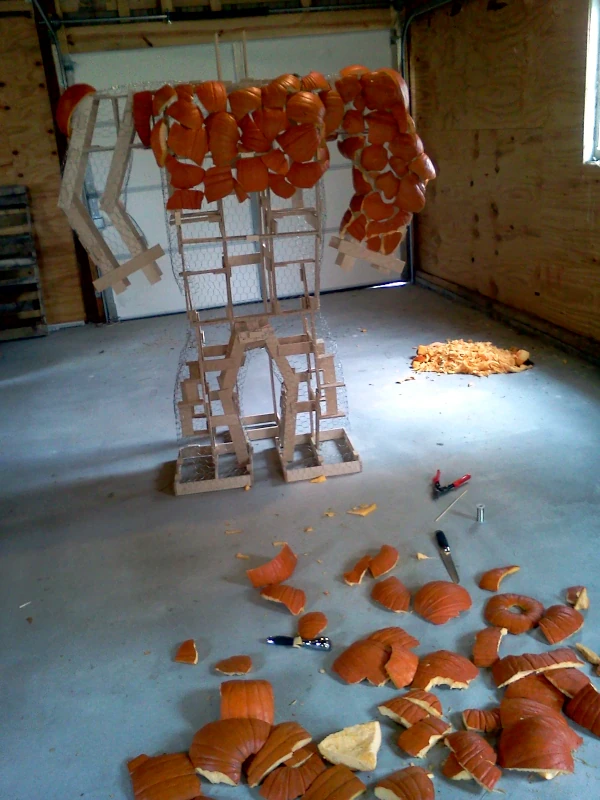 The skeleton partially covered with pumpkins. Piles of pumpkin pieces are on the floor.