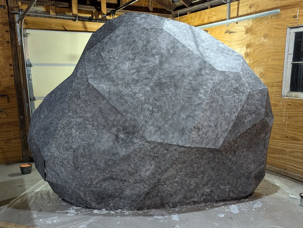 An eight-foot-tall rock, made of cardboard that's been painted a mottled gray.